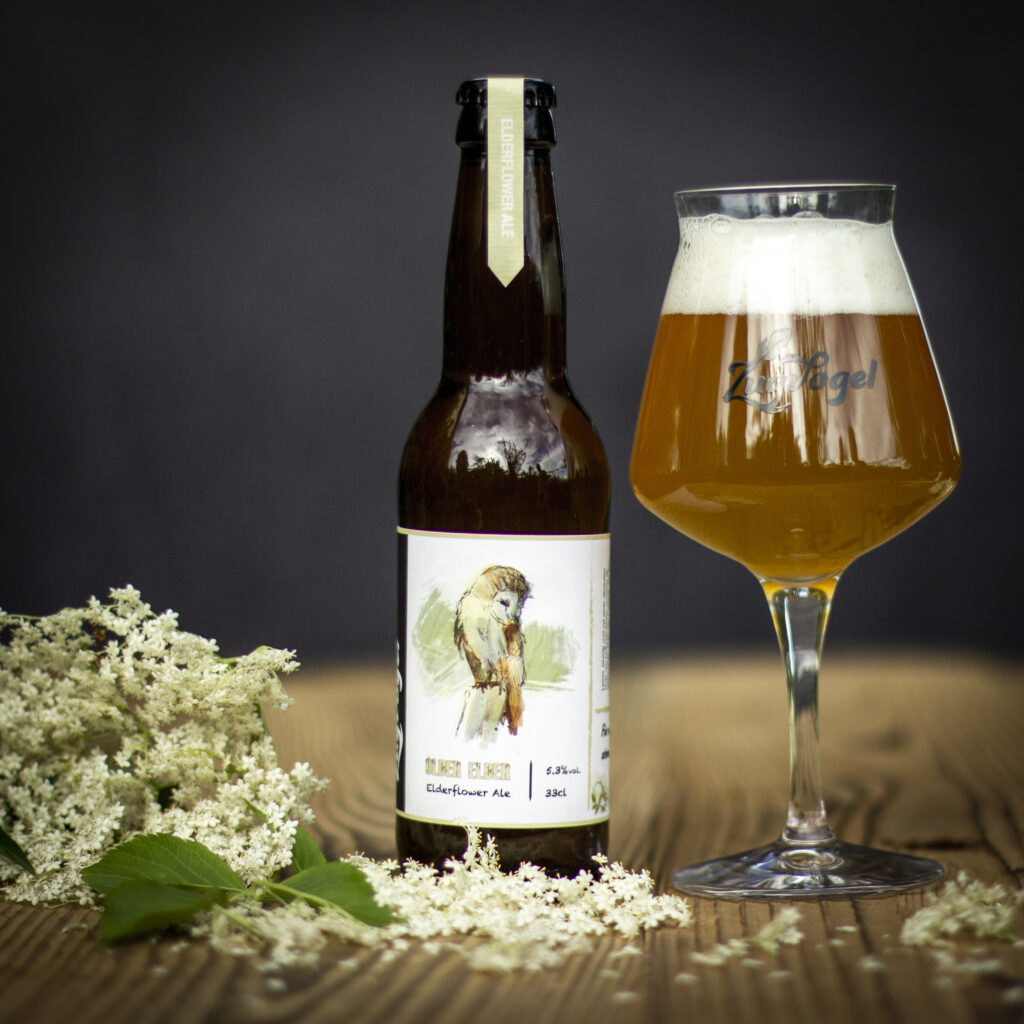 Foto einer Flasche Fond Blond mit einem Glas rechts und Orangen, Koriander und Weizen im Vordergrund